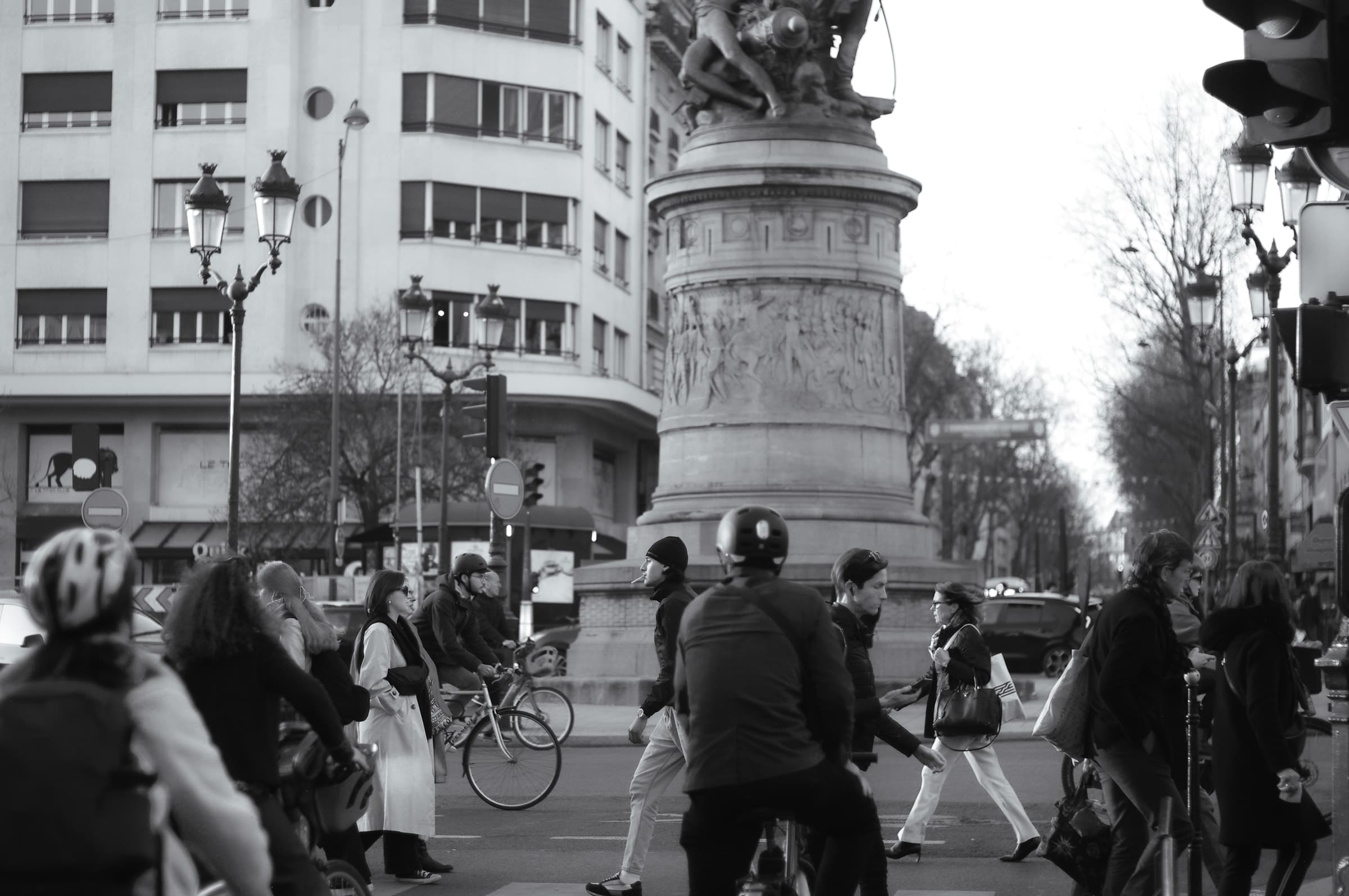 Black-and-white photograph of pedestrians and cyclists around the monument at Place de Clichy, Paris