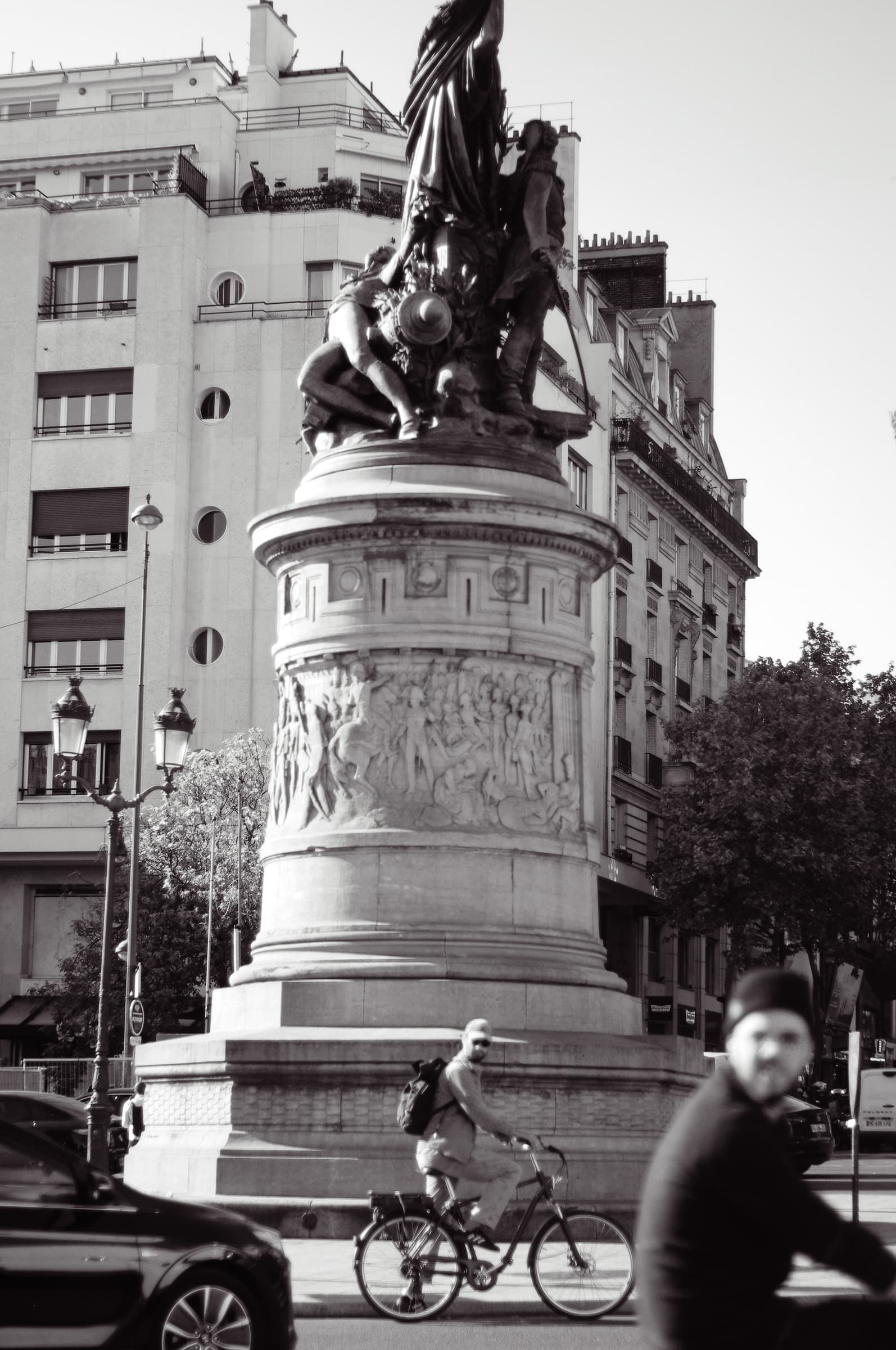 A cyclist and a blurred passerby in front of the monument at Place de Clichy