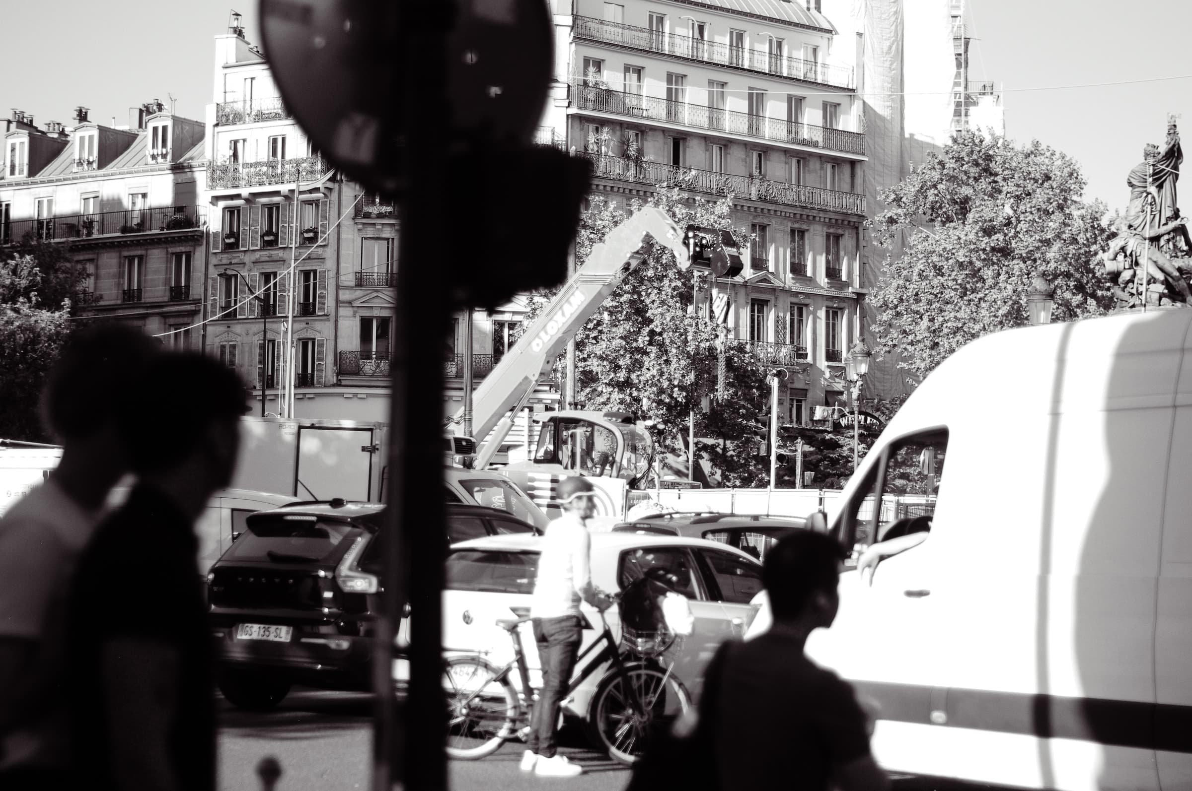 A pedestrian in shadow beside traffic lights, cars, and a white van
