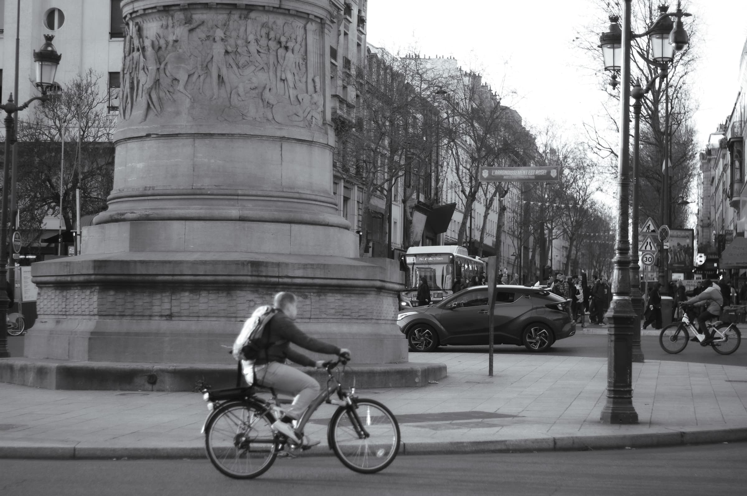 Black-and-white photograph of a cyclist passing the monument at Place de Clichy